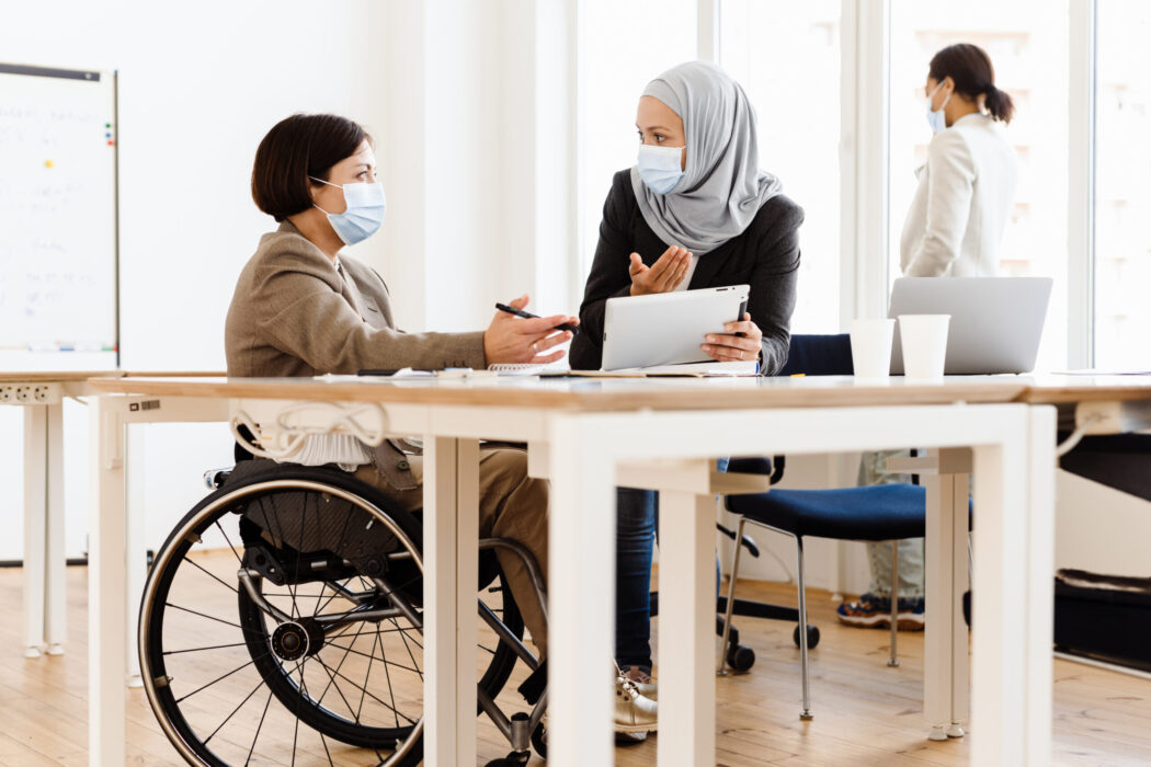 Two women in face masks talking at a table.