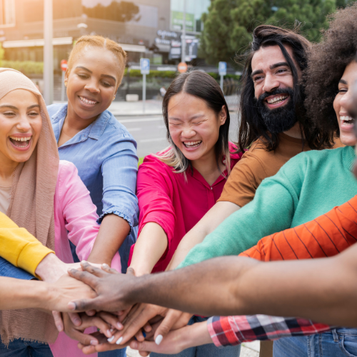 A group of diverse people smiling and putting their hands together in the middle.