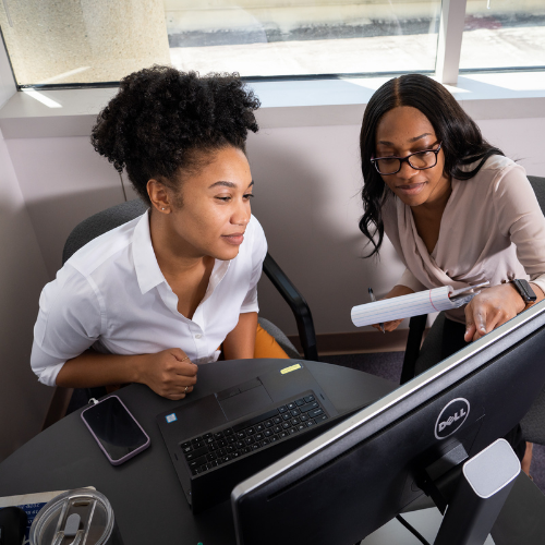 Two women staring at a computer monitor while one of the women point to the screen.