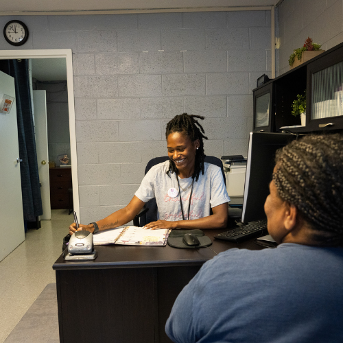 Community health worker writing at a desk while talking to a community member.