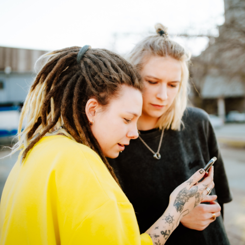 Two androgynous women looking at a phone together.