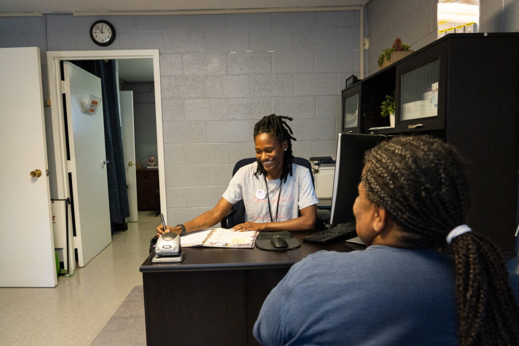 Community health worker writing at a desk while talking to a community member.