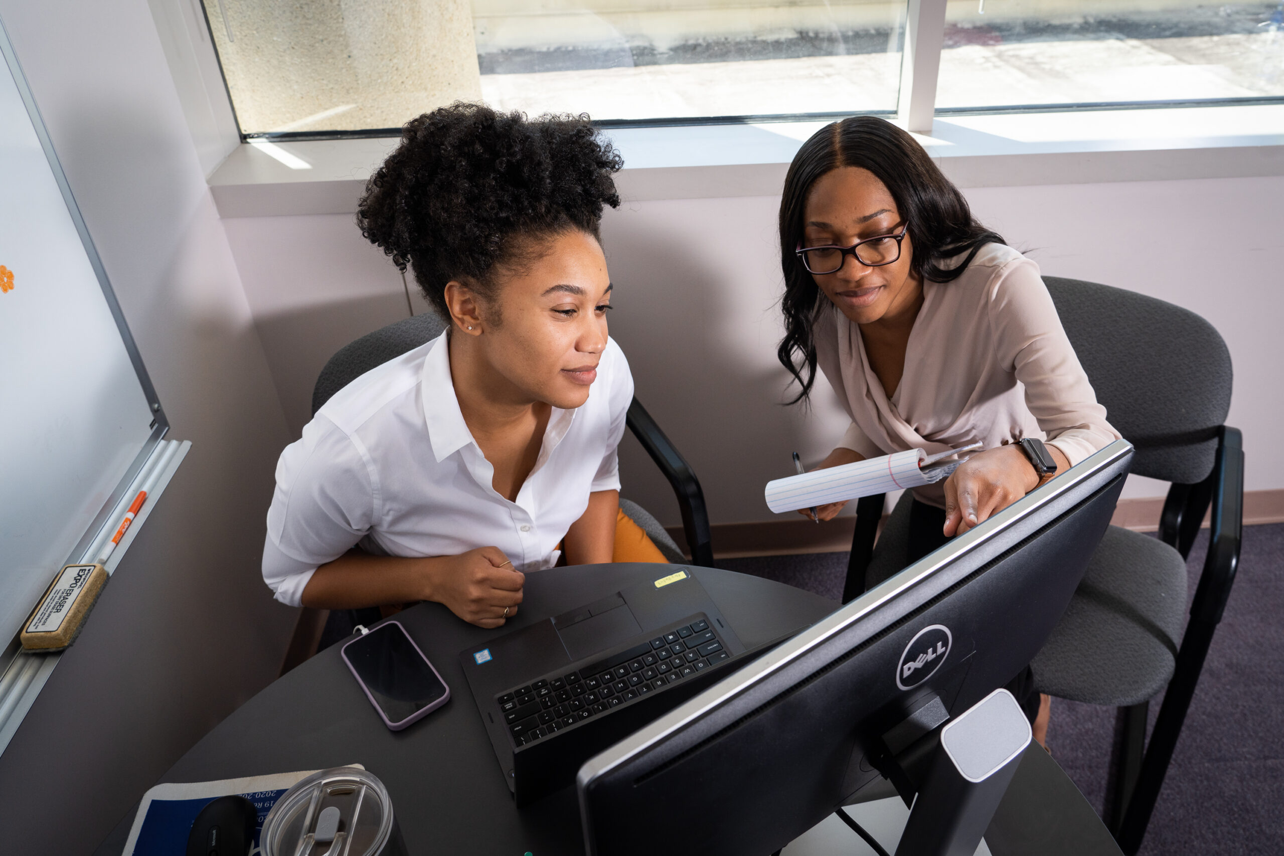 Two women staring at a computer monitor while one of the women point to the screen.