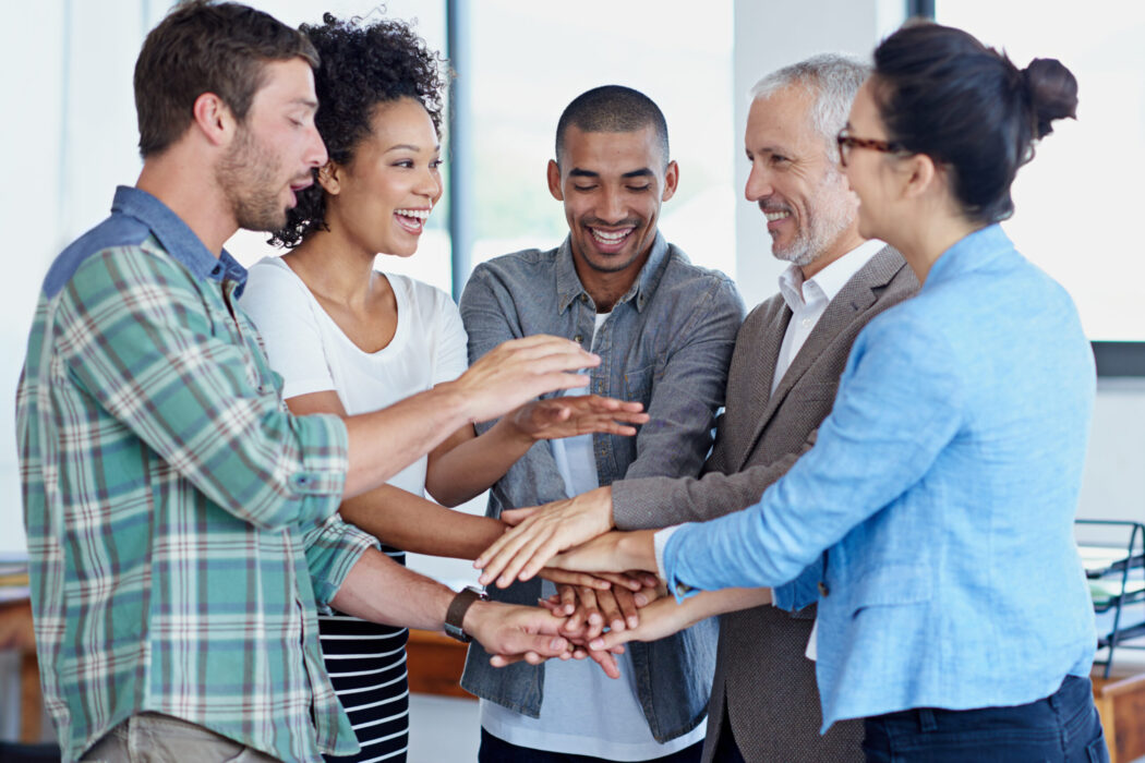 Shot of a group of happy coworkers standing with their hands together in huddle in an office.