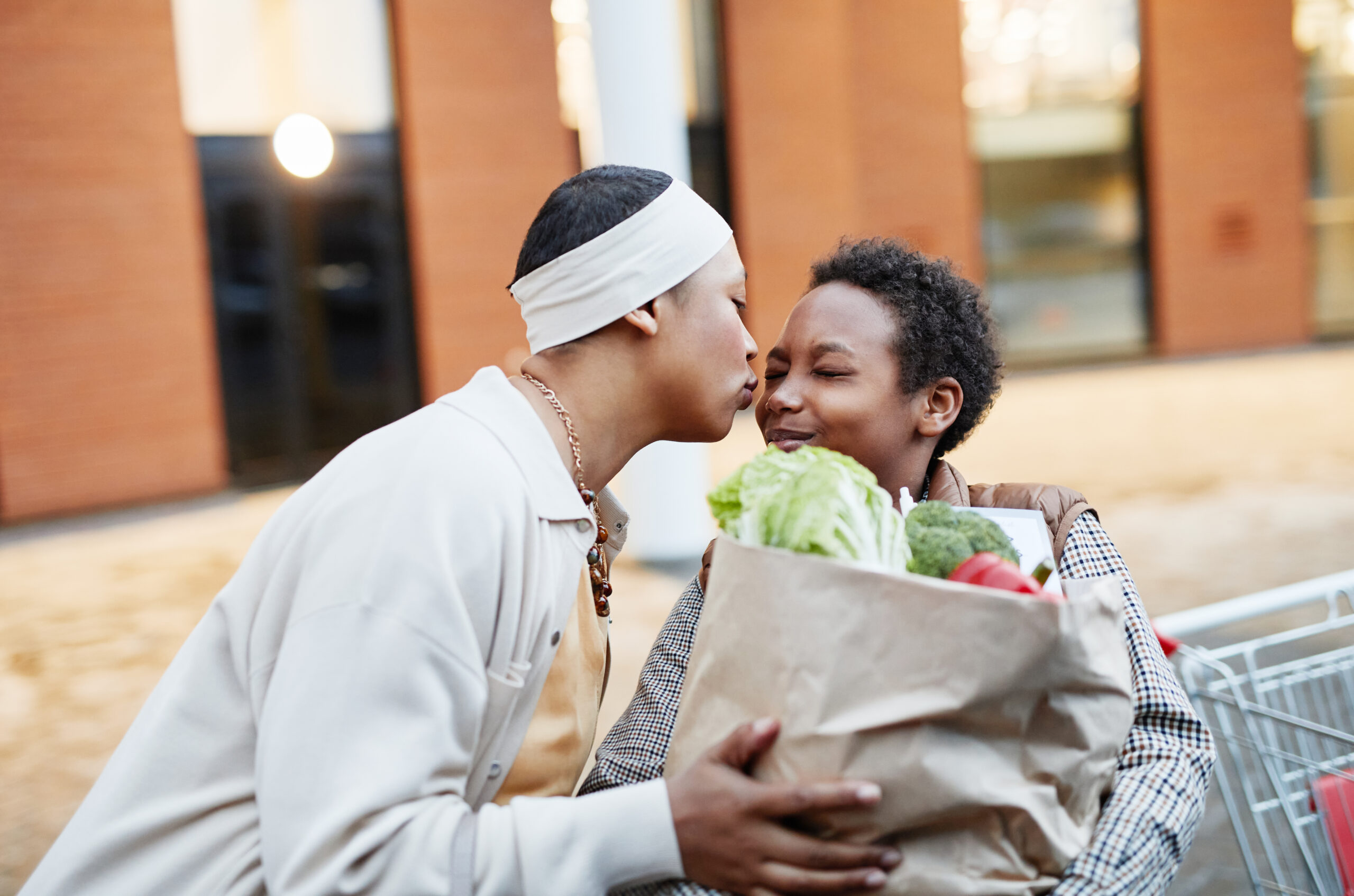 Mom kissing son on the cheek as he helps with groceries.